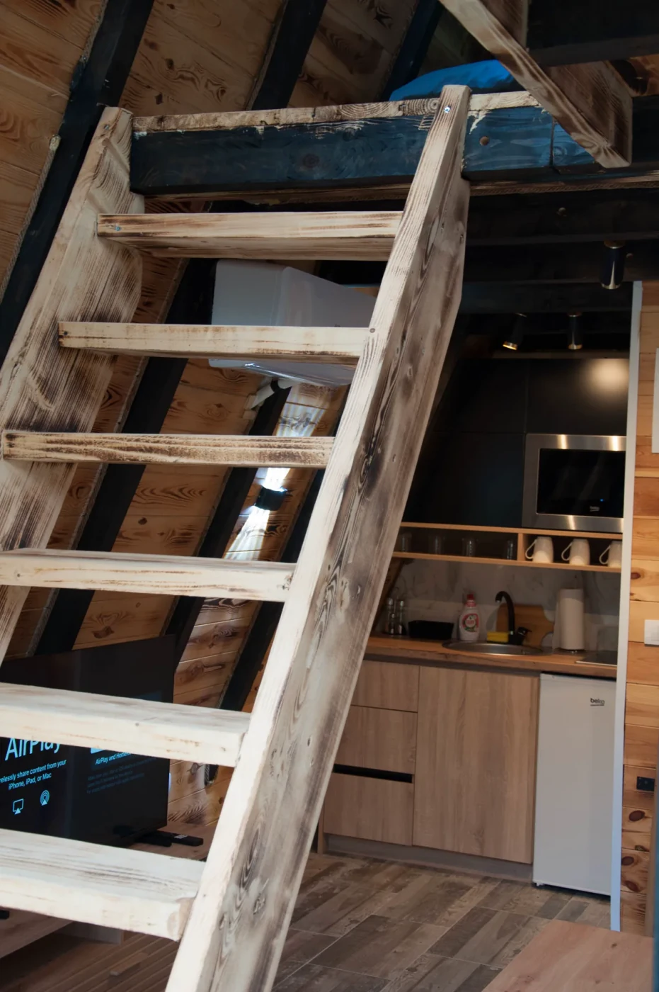 Drvene stepenice ka potkrovlju i kuhinjski kutak A-frame vikendice